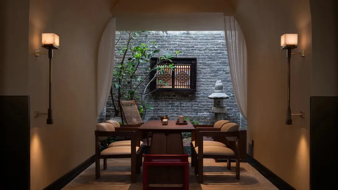 A modern dining room with a wooden table and chairs, surrounded by a brick wall, with a vase on the table, in a dimly lit space