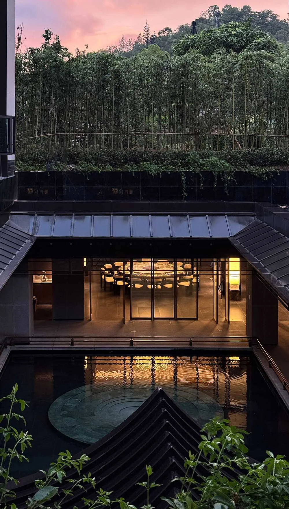 A dimly lit modern room with a pool in the center, surrounded by furniture and decorated with wood and glass materials