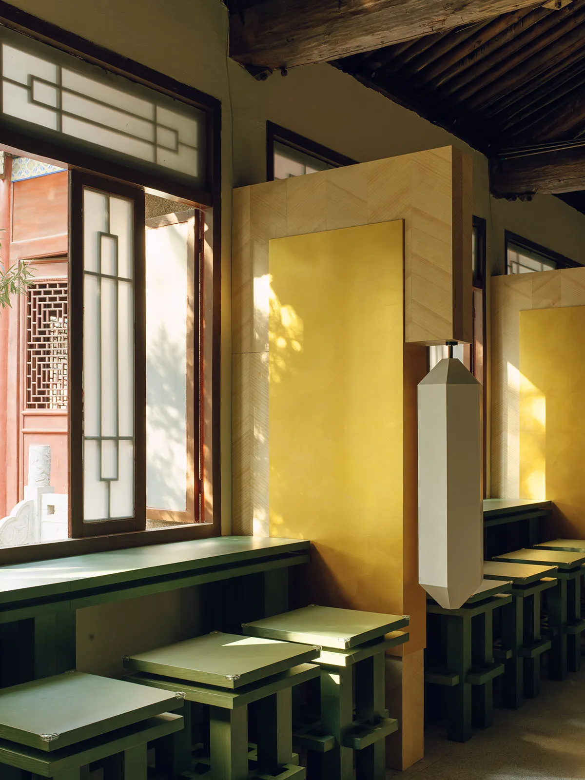 A modern restaurant with a yellow and green color scheme, featuring wood furniture and large windows for natural light