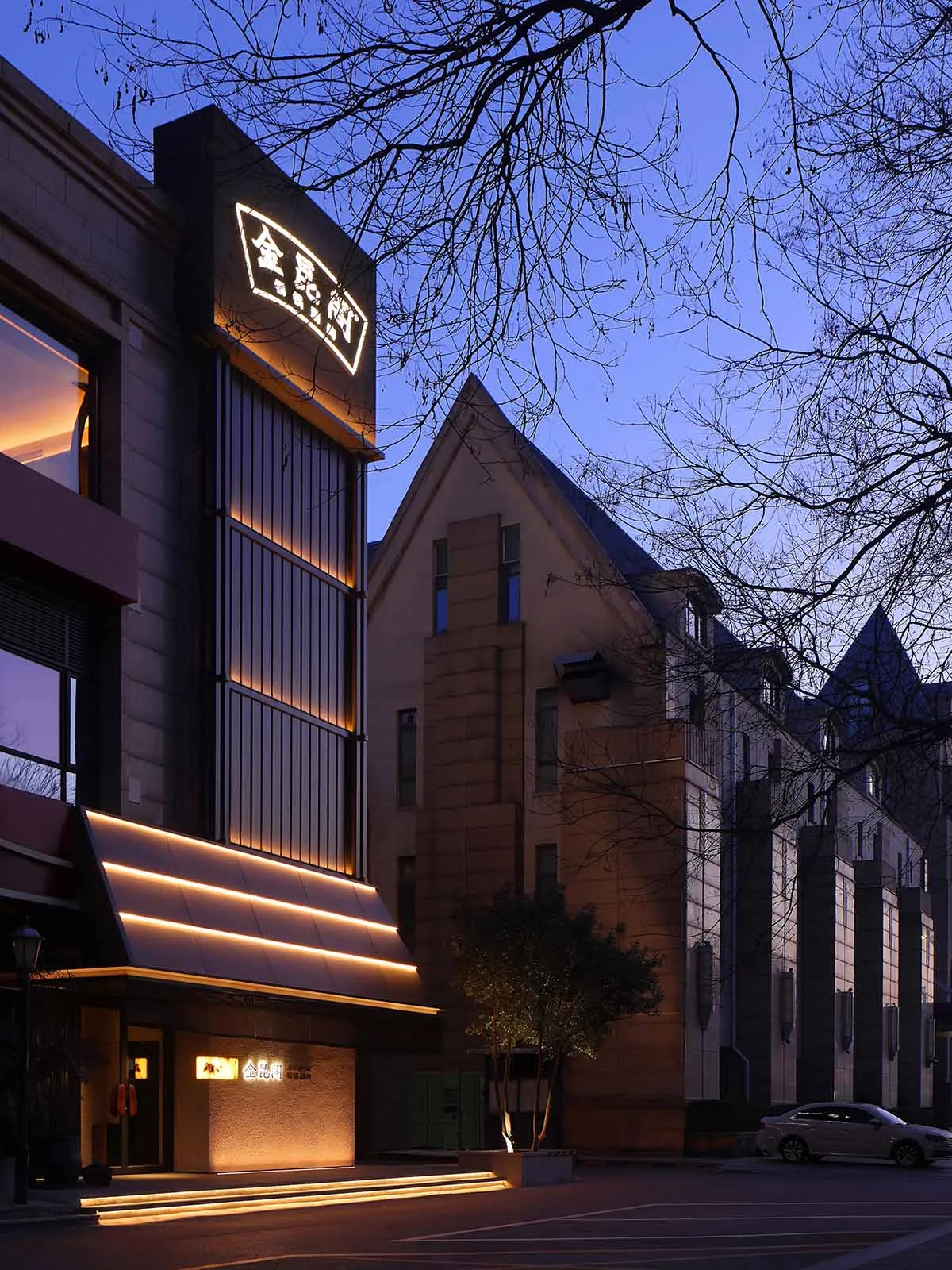 A city building with a brick facade and a prominent archway illuminated by a light source, set against a darker urban backdrop