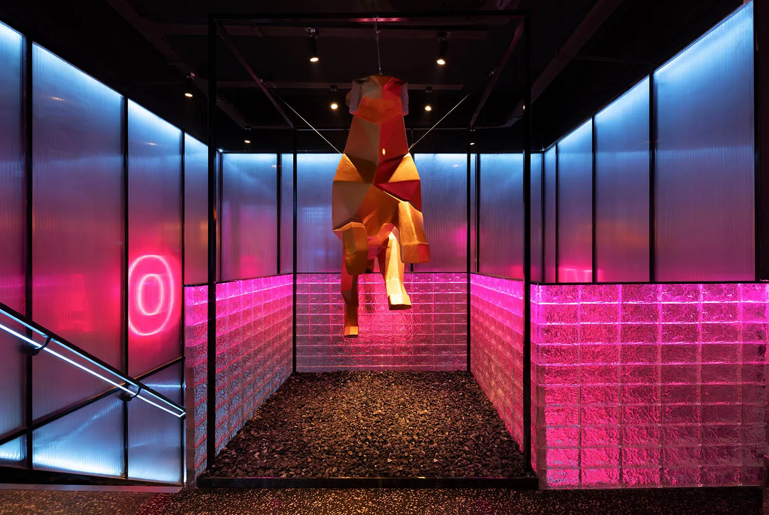 A modern room with a pink and black color scheme, featuring a staircase with a pink railing, a red wooden horse sculpture hanging from the ceiling, and a unique artistic touch