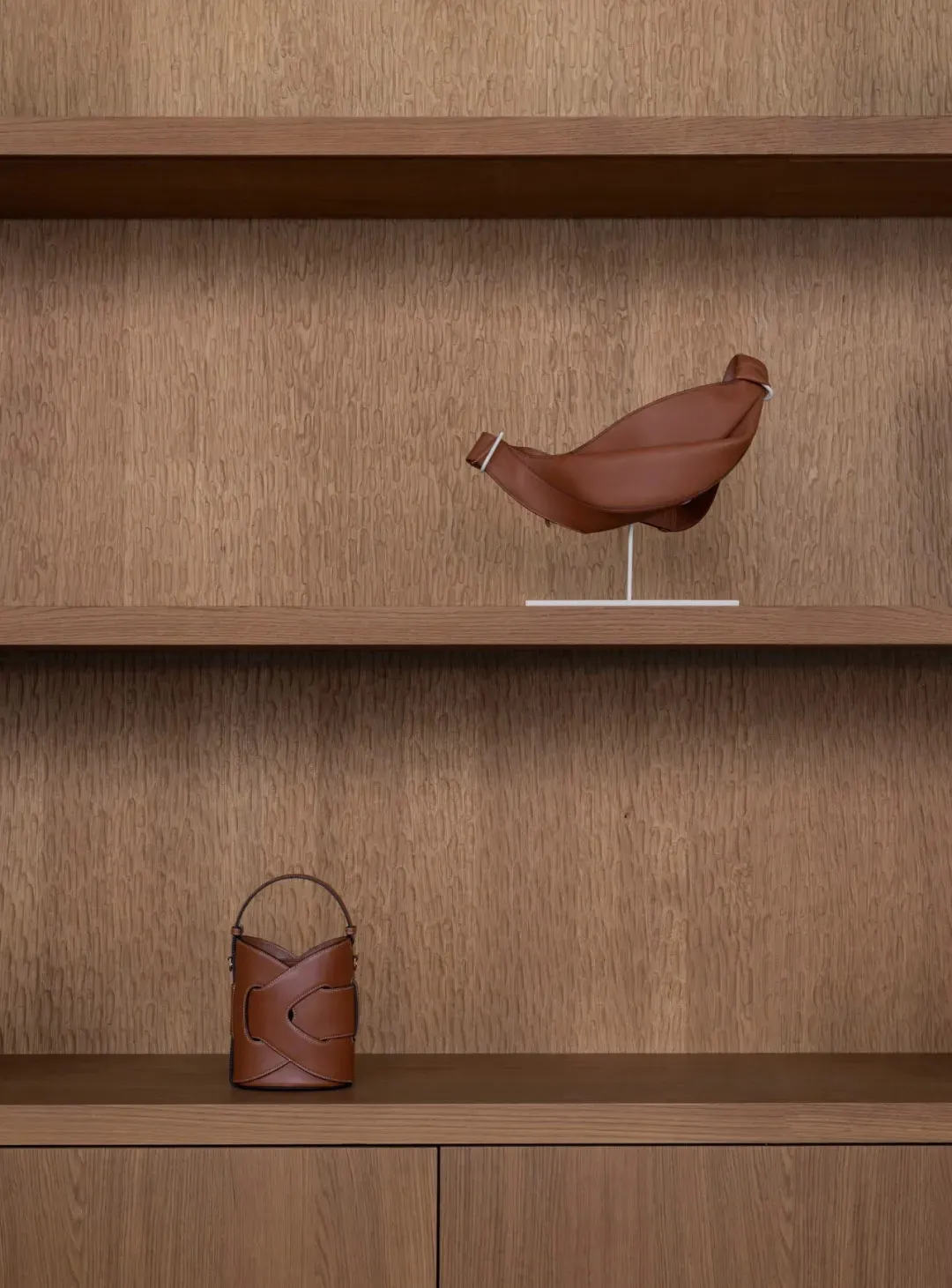A wooden shelf with a brown leather bag and two smaller bags, set against a neutral background, with natural light creating a warm atmosphere
