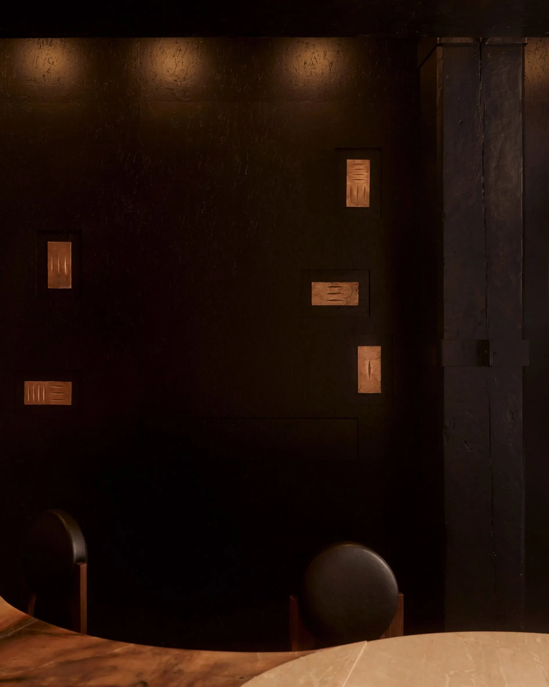 A small, dark room with a black wall and a black chair in the center, creating a minimalist atmosphere