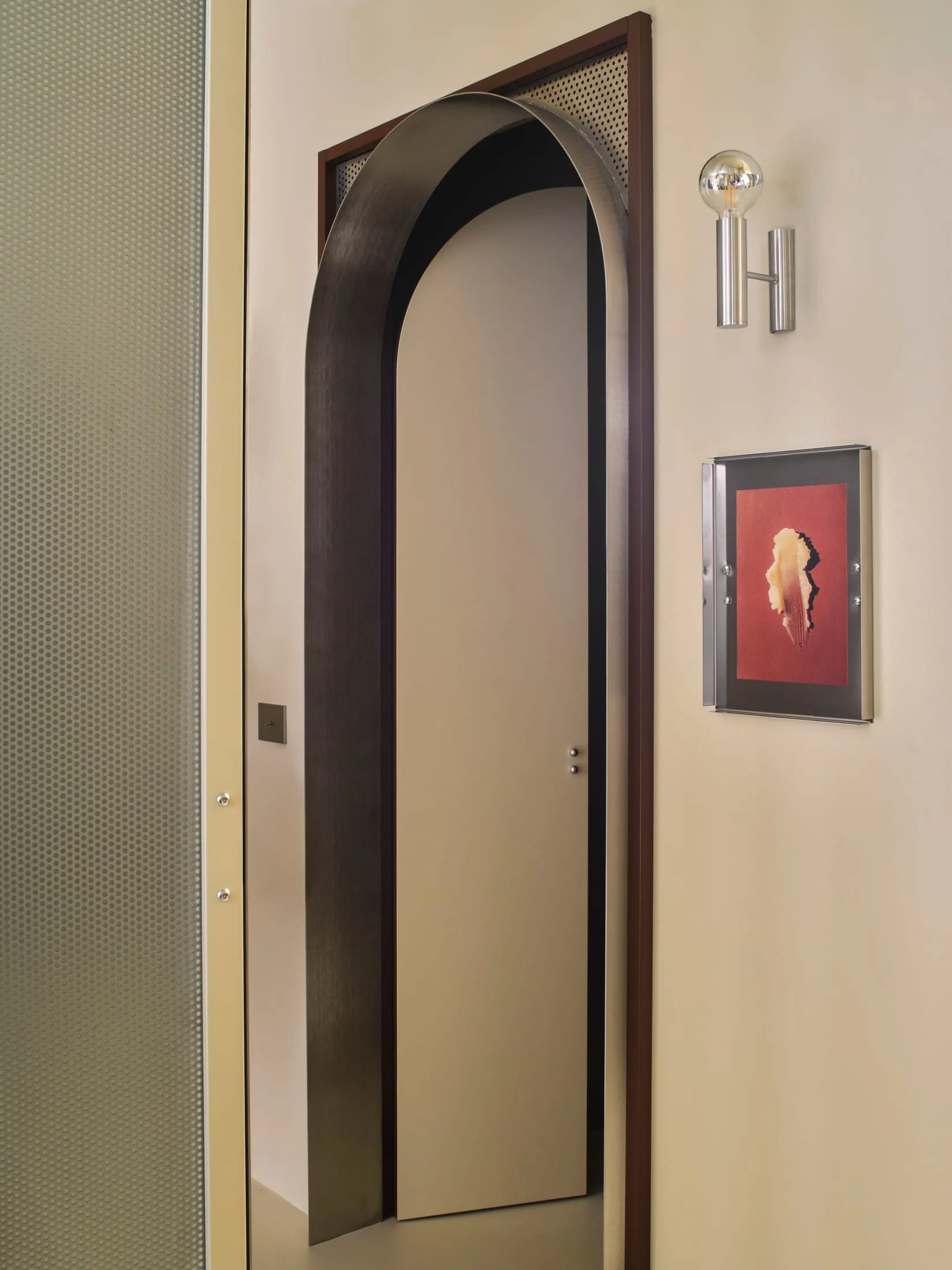 A wooden doorway with a glass door, adorned with a picture, leading to a bathroom with a mirror