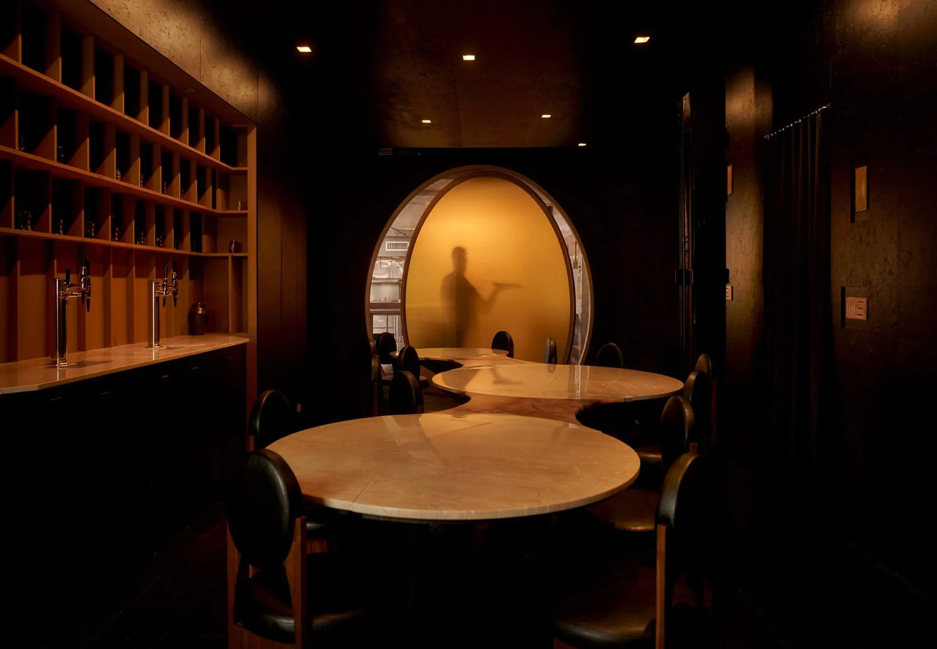 一間餐廳用餐區域，擺放著一大圓桌、葡萄酒杯和服務生，周圍為木材和玻璃元素，四周的燈光溫暖柔和