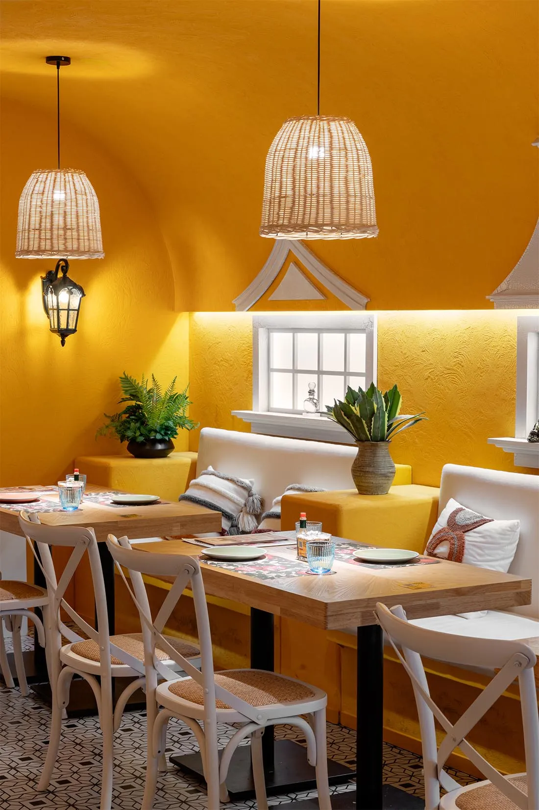 Dining area with yellow walls, white furniture, and potted plants, illuminated by natural light