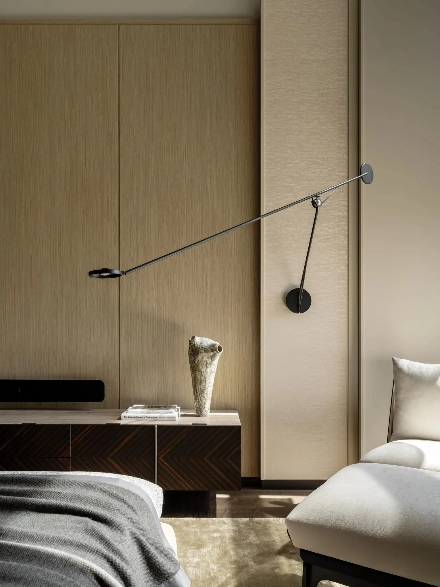 Cozy bedroom with a bed, dresser, and lamp, featuring a wooden floor and tan color scheme, with natural light from a window