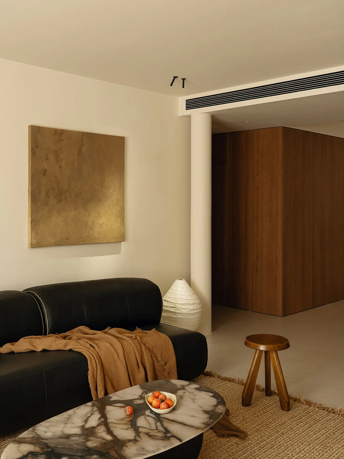 Cozy living room with a black couch, chair, and dining table, featuring a white wall, brown wooden door, and decorative elements