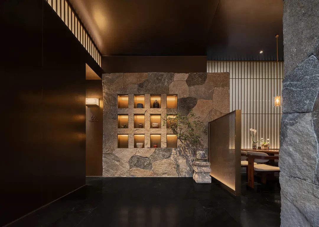 Dining room with a stone wall and floor, a modern dining table and chairs, vases, and dim lighting creating a cozy atmosphere