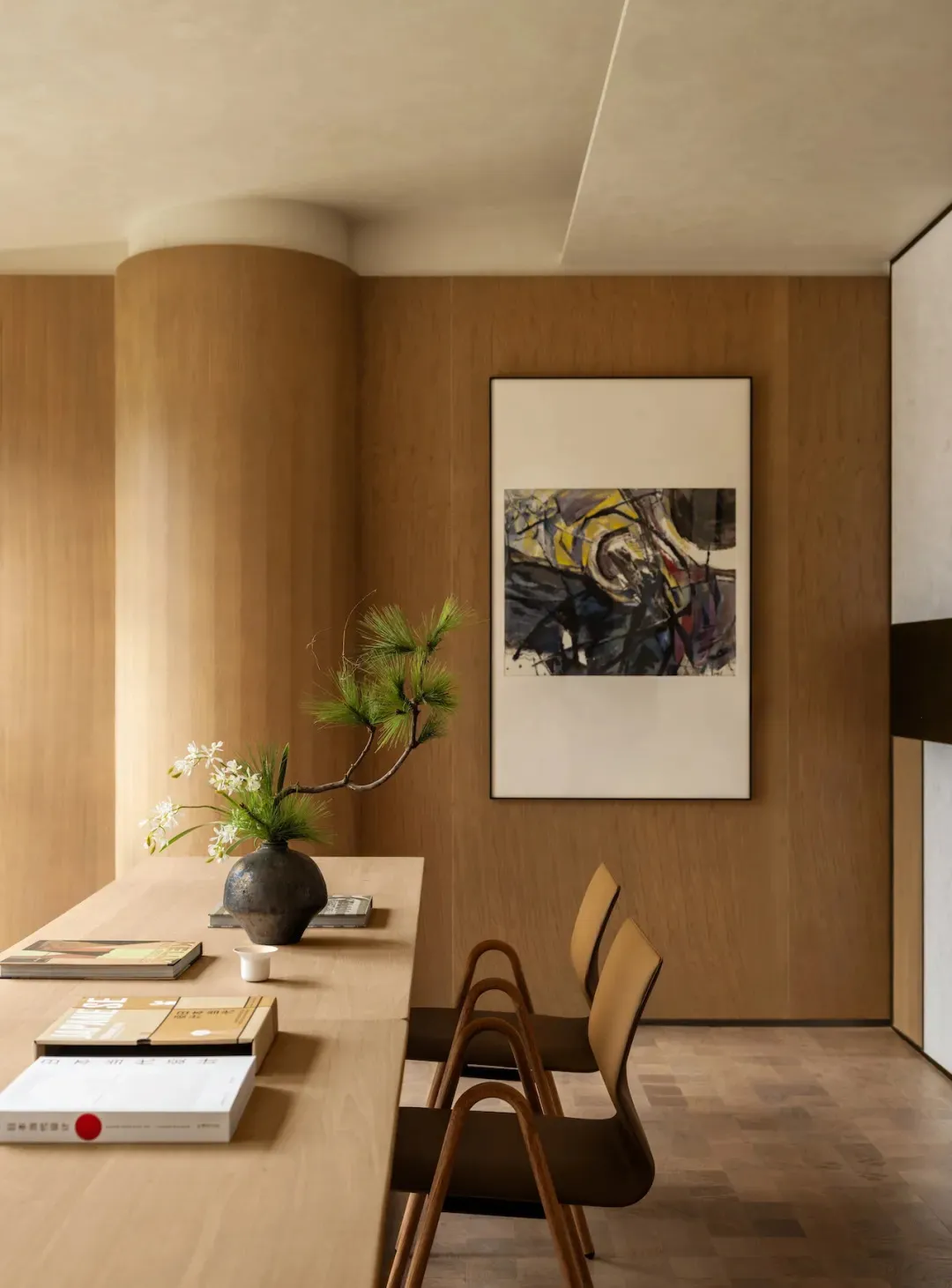 Warm and inviting living space with wooden floors and walls, featuring a dining table, chairs, a potted plant, and a painting on the wall