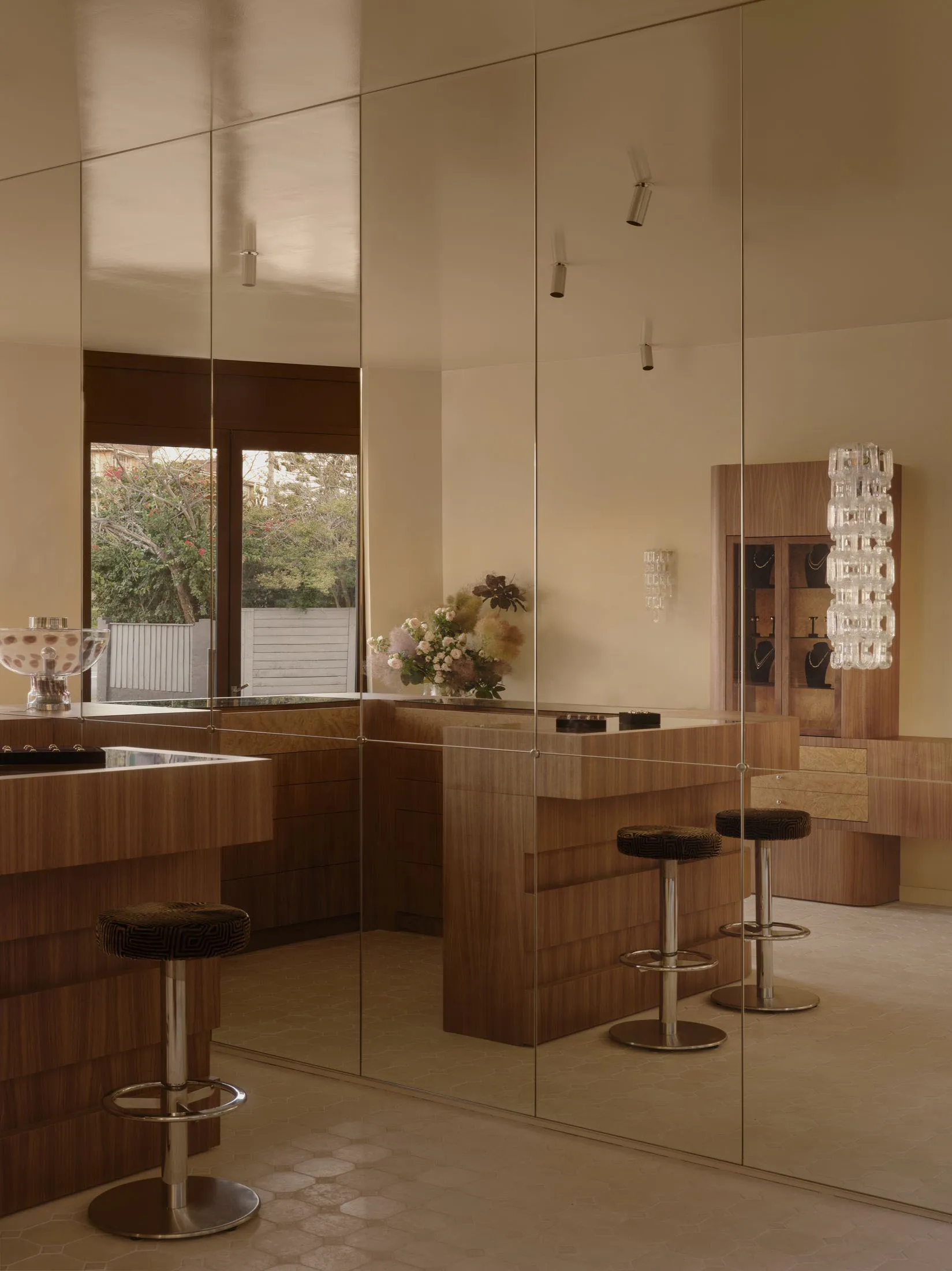 Modern kitchen and dining space with a large island, wooden furniture, and glass accents, decorated with a potted plant and vases, lit by natural sunlight
