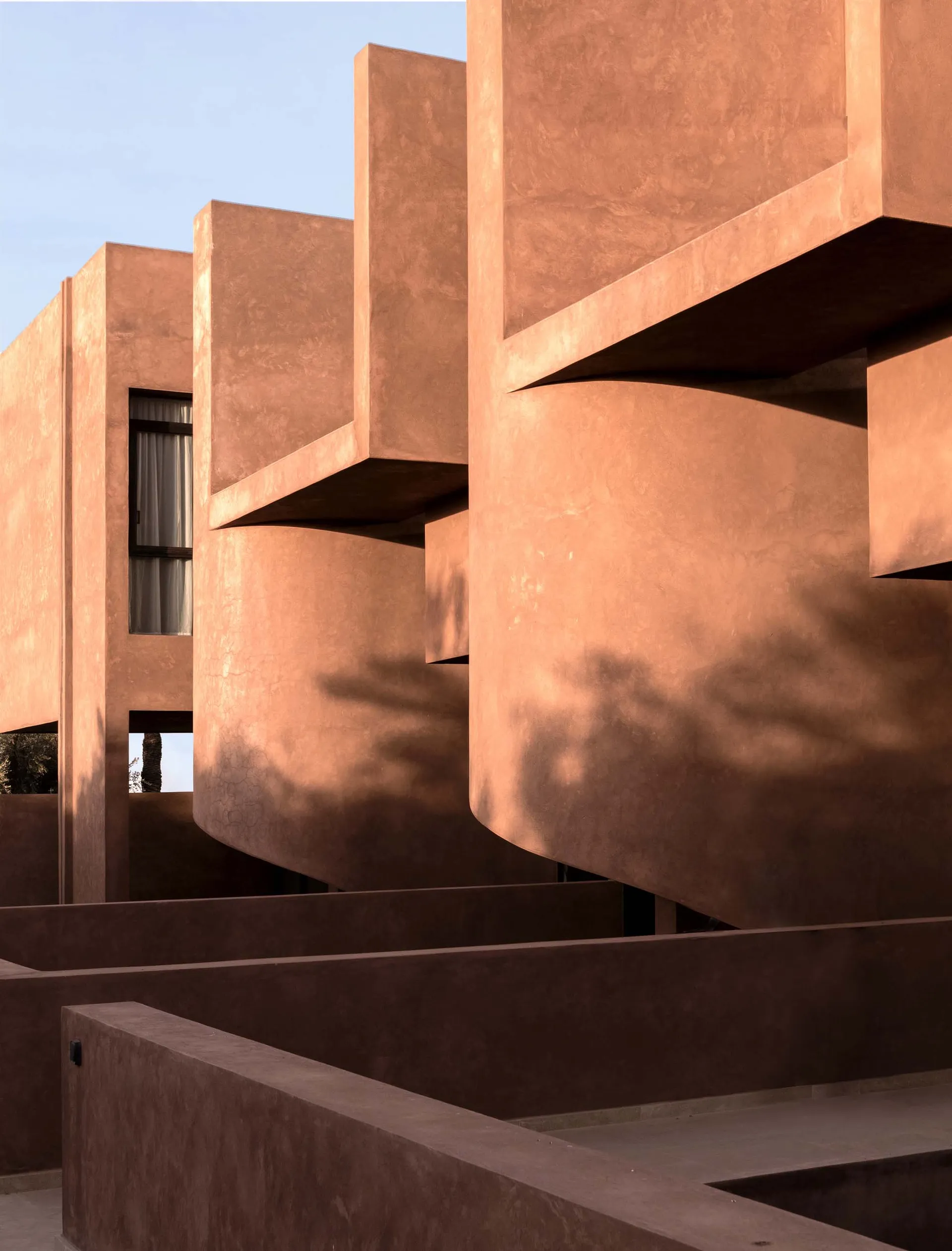 A serene outdoor space with a red brick building featuring a unique curved design and staircase, set in a calm courtyard or public area