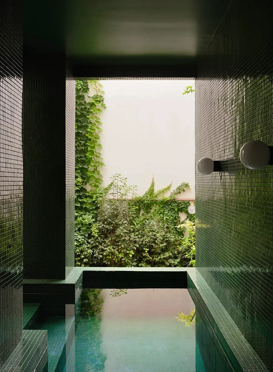 A modern bathroom with a green tile floor, a glass shower door, a sink, and a toilet, well-lit and inviting