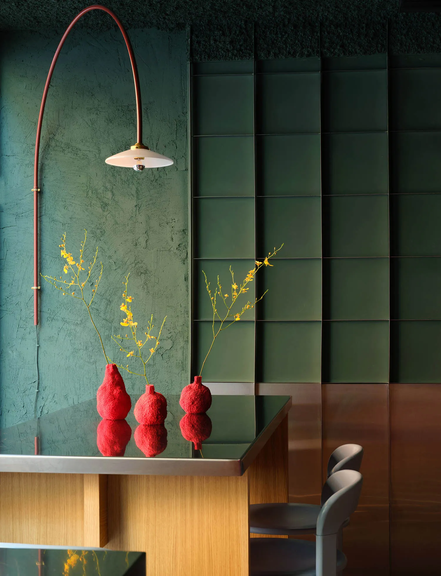 A modern living room with a green accent wall, a dining table, and comfortable seating, decorated with flowers and a potted plant