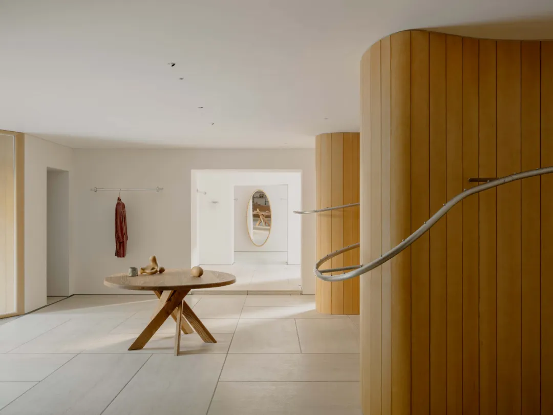 A warm and cozy room with a wooden floor, white wall, and wooden staircase and table, featuring a mix of natural and artificial lighting