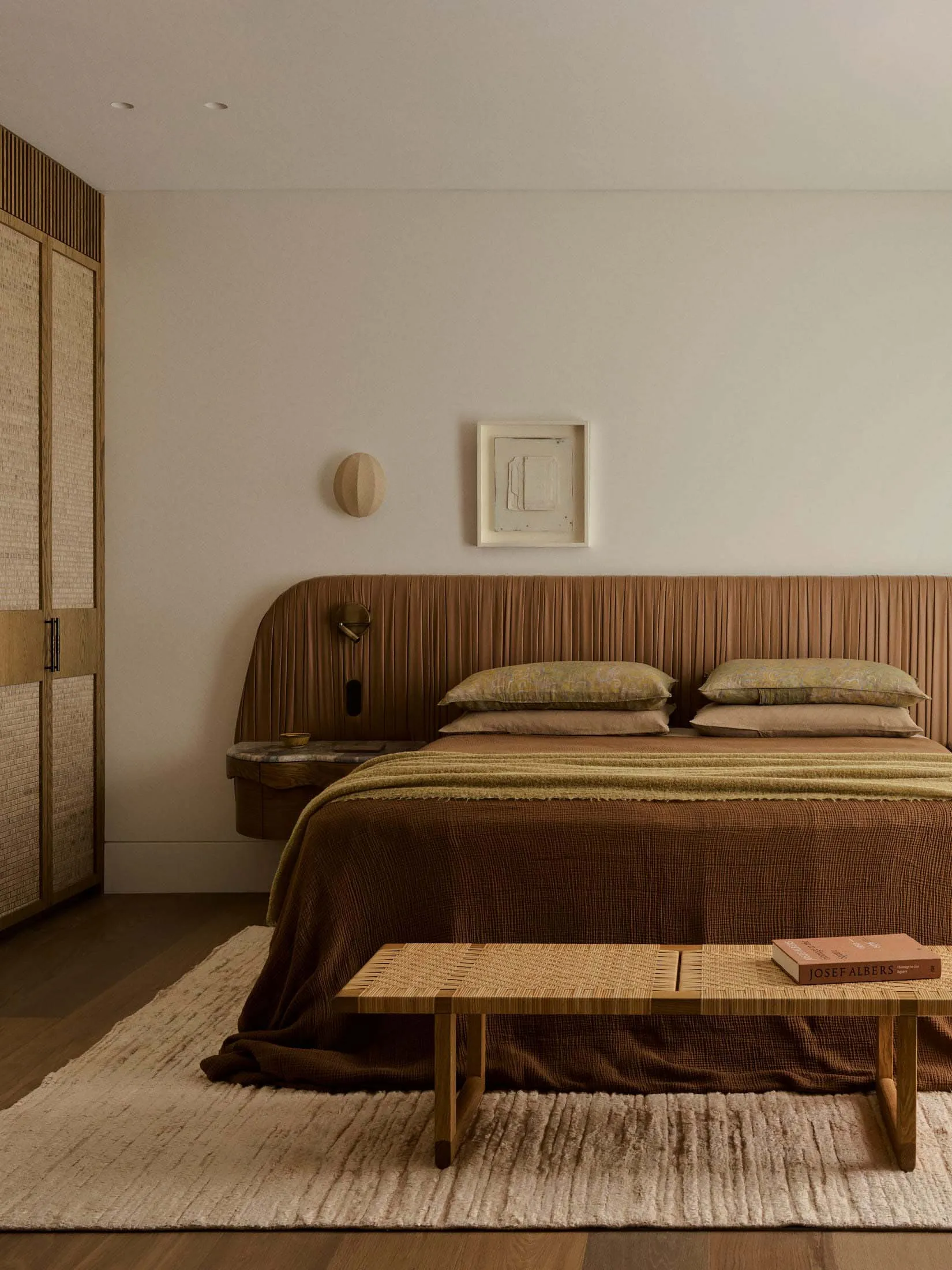 Cozy bedroom with a brown bed, table, and chair, surrounded by warm wood tones and natural light