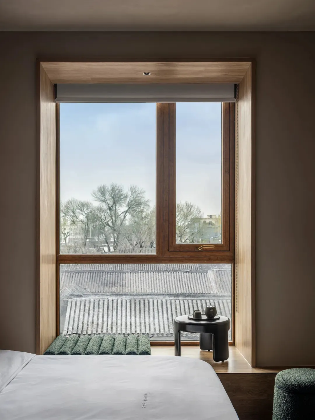 Cozy modern bedroom with a large window, a bed, and natural light, decorated with a vase and a bowl, and a chair and dining table