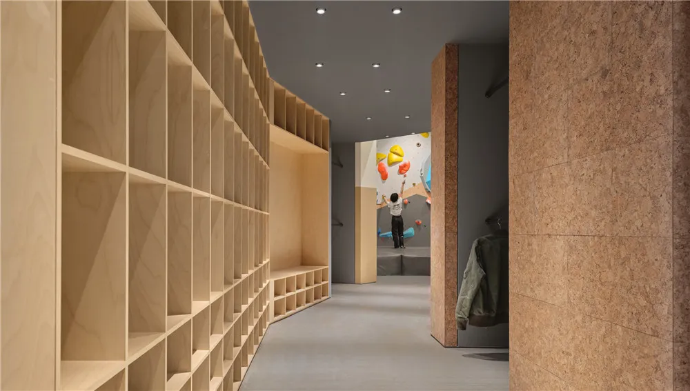 Cozy modern room with a wooden floor, a painting of a person climbing a wall, a bench, bookshelf, and jacket, dim lighting