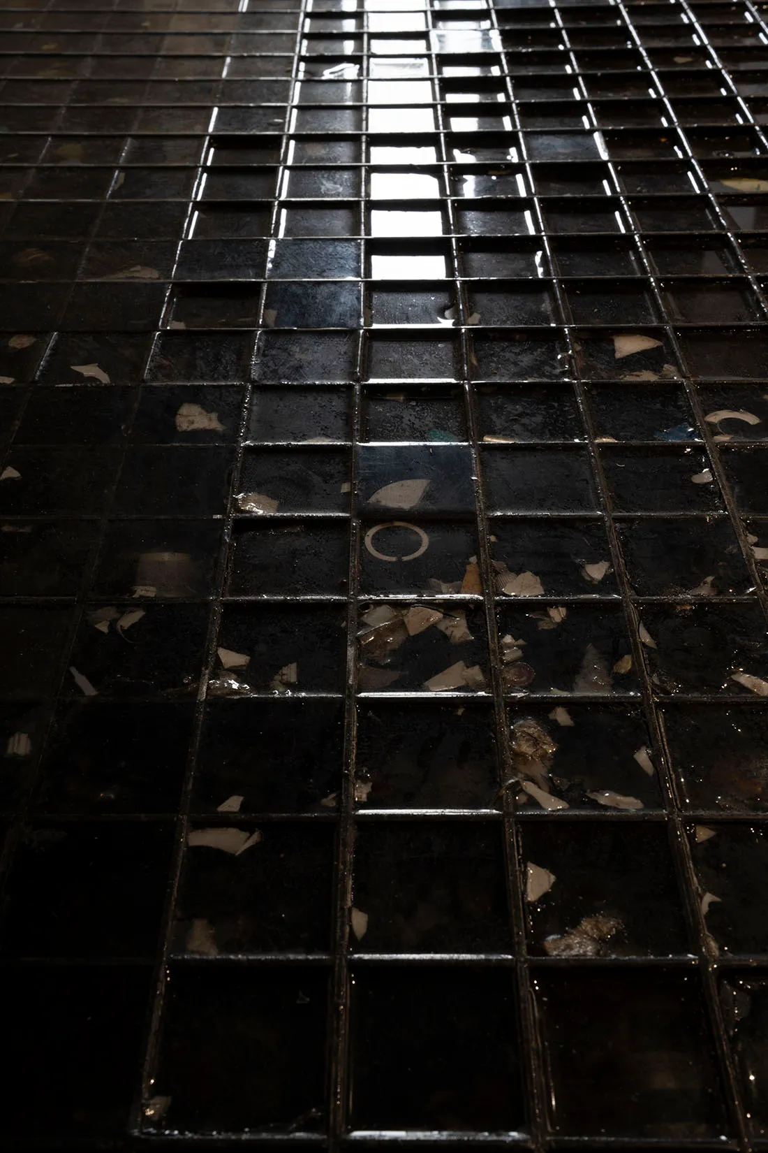 A dimly lit black and white photograph of a tile floor, possibly in a bathroom, with a minimalist and functional style