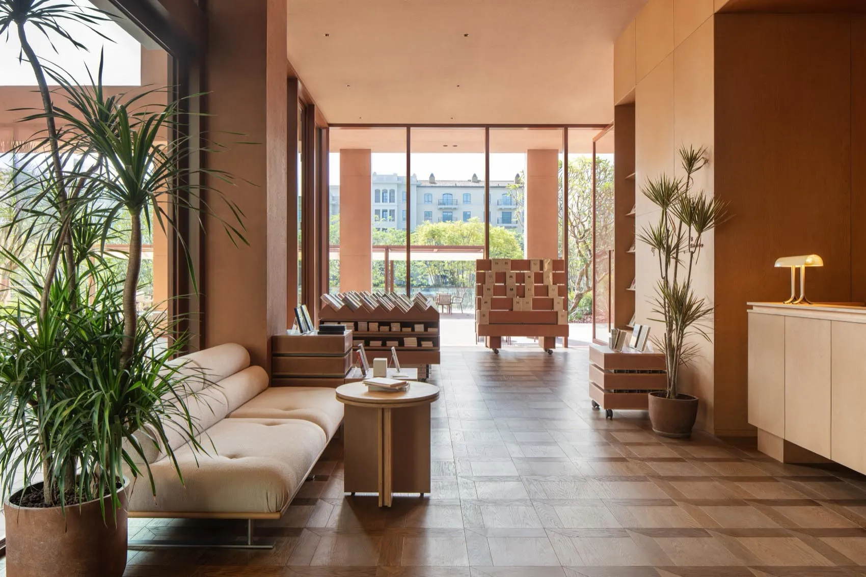 Cozy living room with a couch, coffee table, bench, books, and a potted plant near a large window