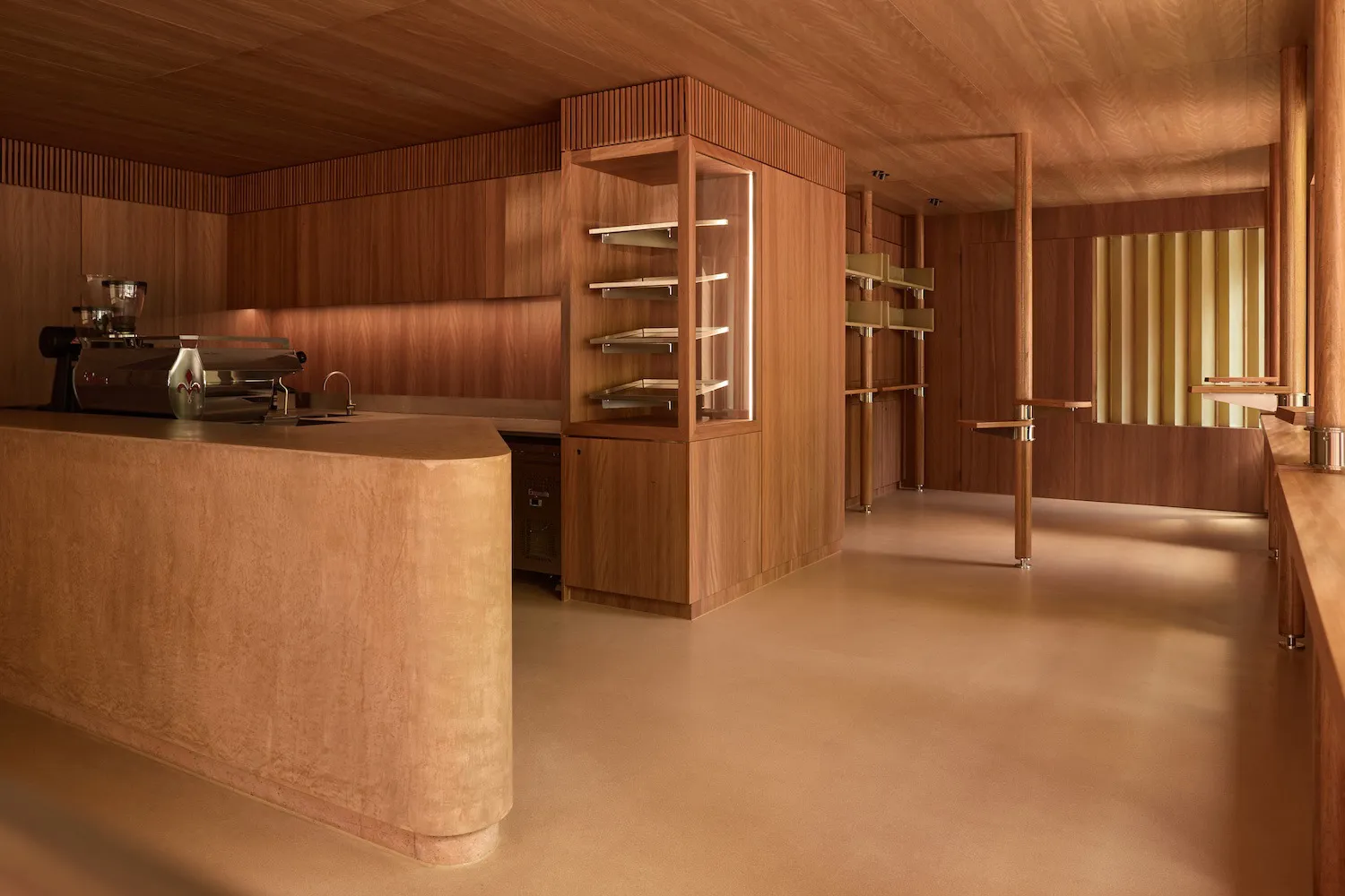 Modern kitchen with wooden floors and cabinets, featuring a sink, refrigerator, and microwave, with natural light and a warm atmosphere