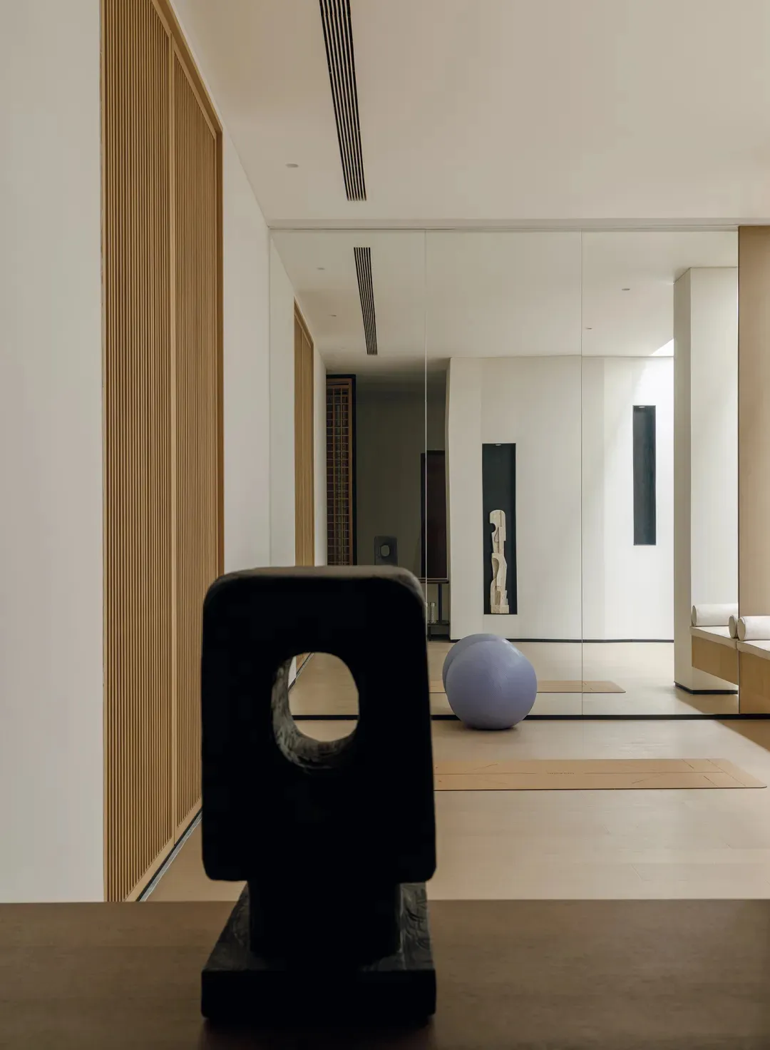 A modern art gallery with a wooden floor, featuring a black sculpture, a purple ball, and a bench in a black and white space with a timeless and elegant atmosphere