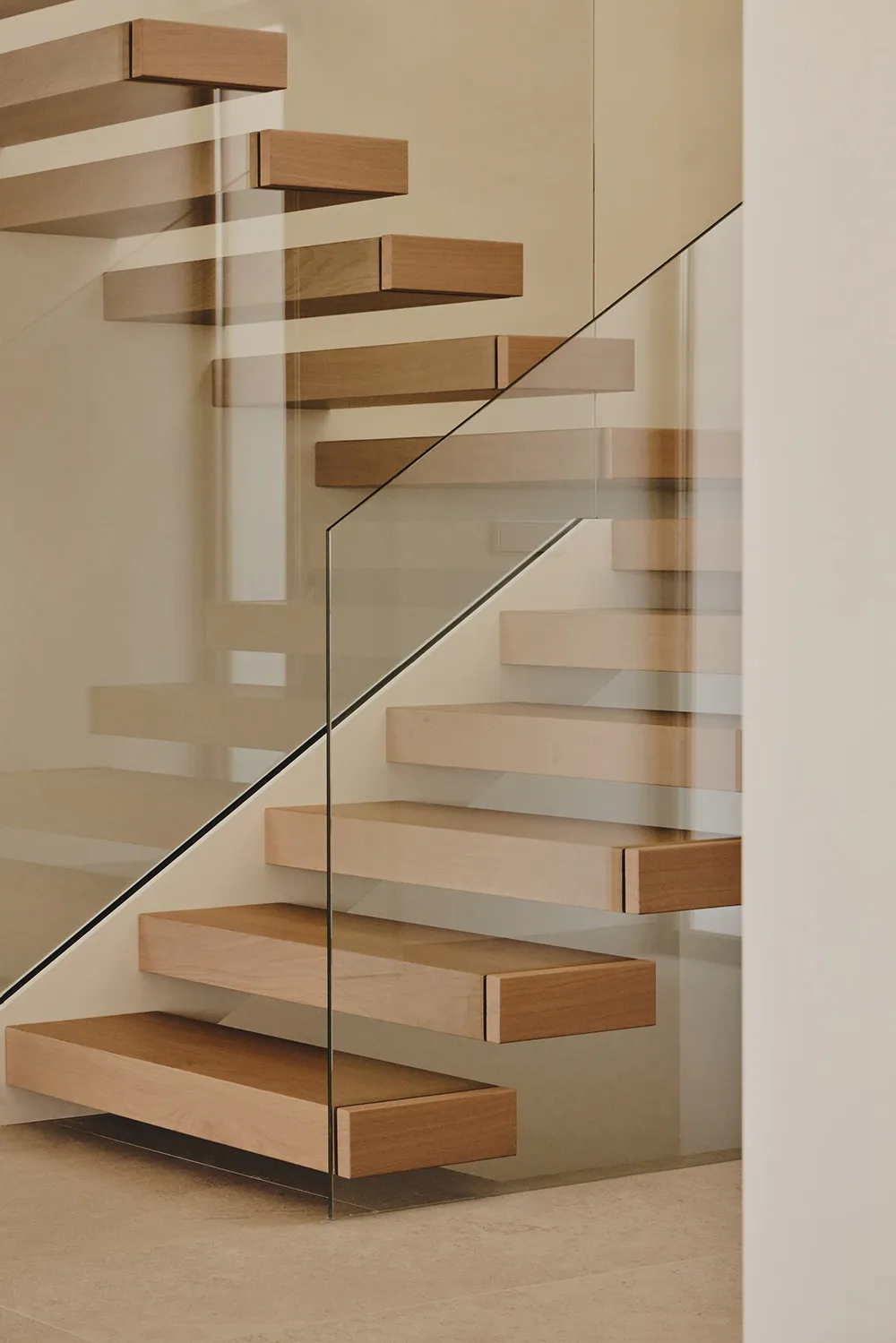 A wooden staircase with a glass railing in a bright and airy room with a white wall, creating an elegant and sophisticated atmosphere