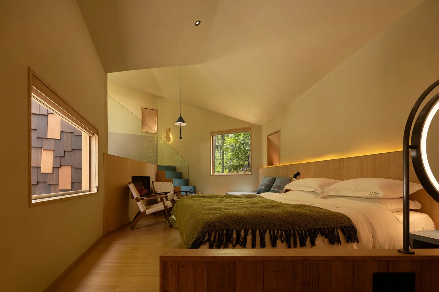 A well-lit bedroom with a wooden floor, a bed, a chair, and a window, creating a comfortable atmosphere