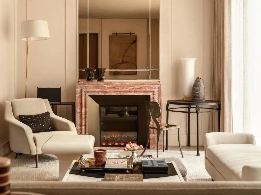 Cozy living room with a fireplace, couch, chair, and coffee table, surrounded by neutral colors and minimal decorations, with natural light from the windows