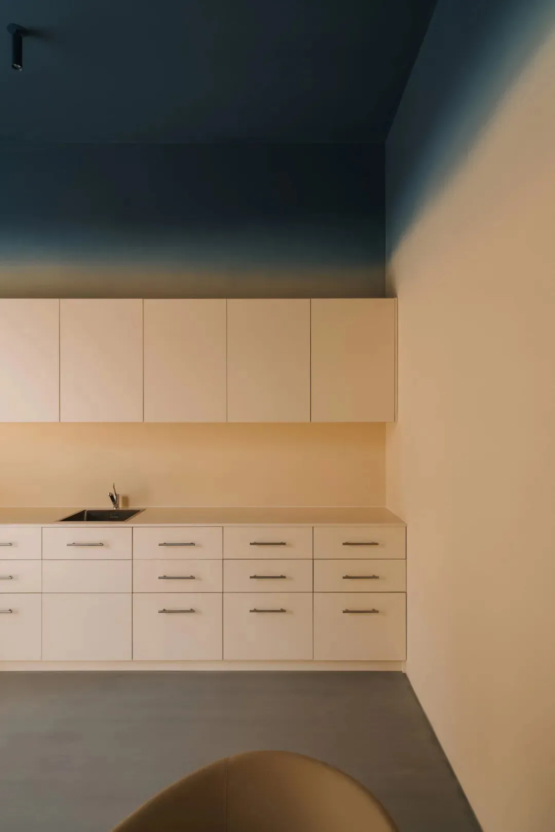 A modern kitchen with white wood cabinets, a marble countertop, a sink, and a cupboard, lit with dim lighting creating a cozy atmosphere