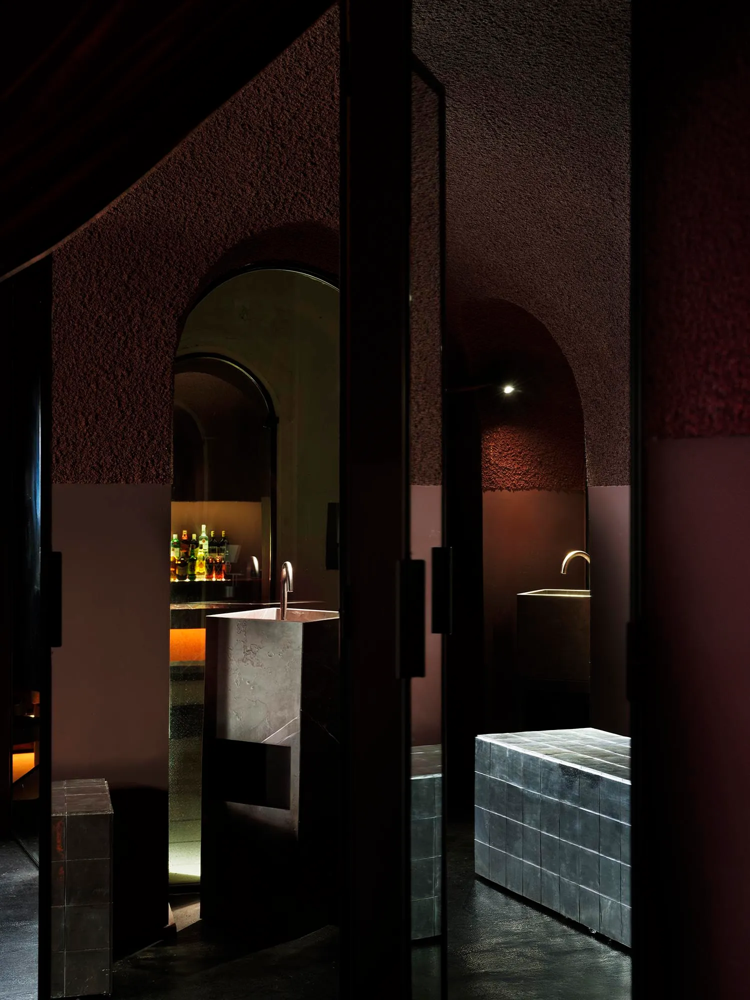 Bathroom with a stone-like appearance, featuring a sink, mirror, and shower, with dim lighting creating a cozy atmosphere