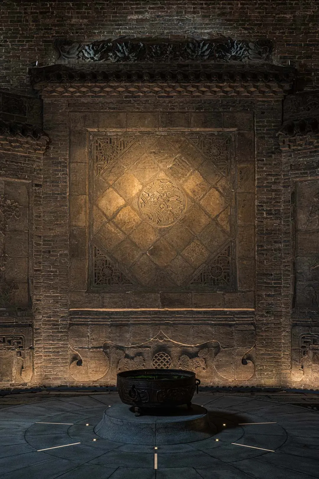 A stone wall with a stone bowl or vase on it, set in a darkened environment with dramatic shadows and textures