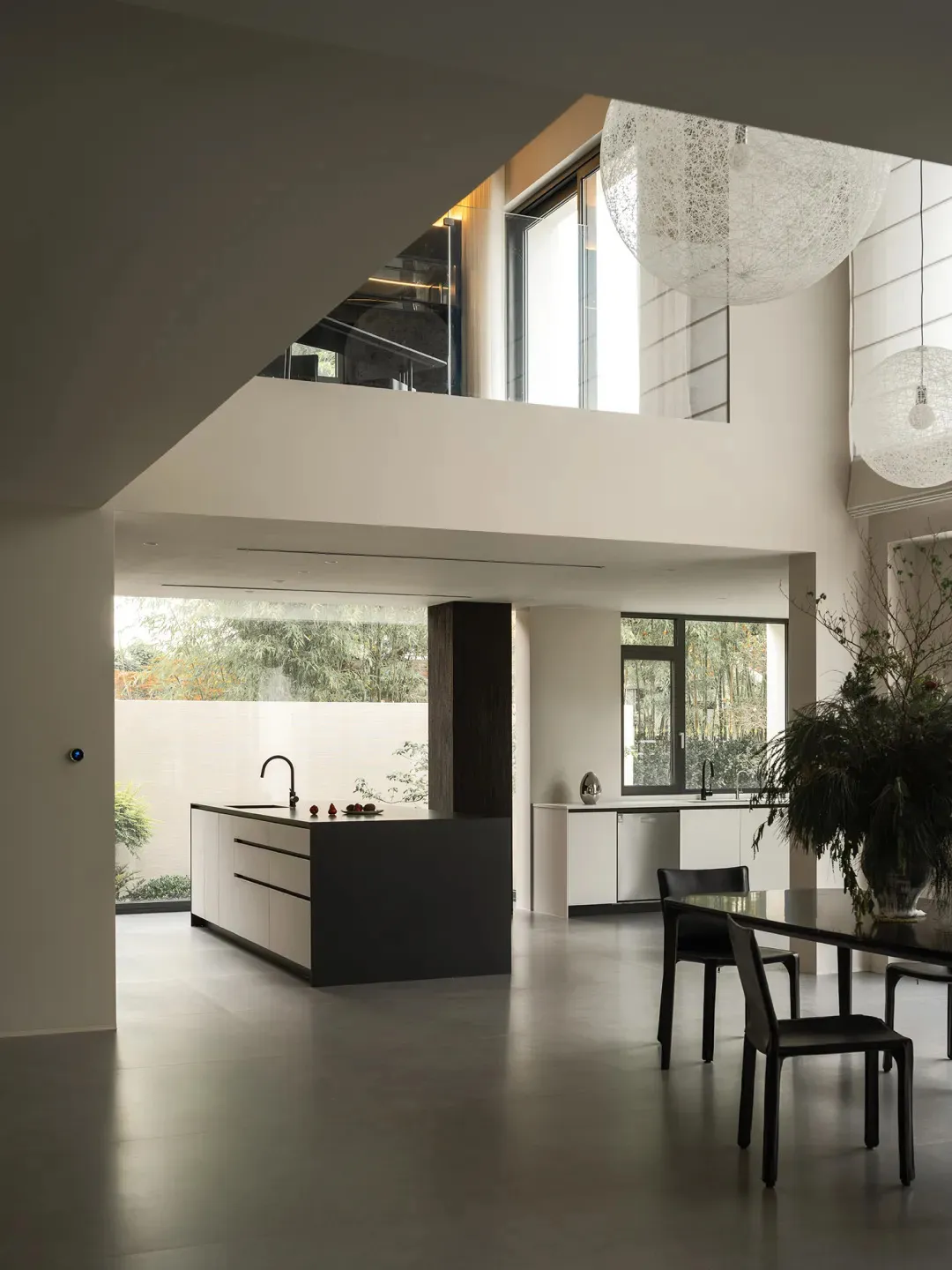 Modern kitchen with a dining area, featuring white walls, grey countertops, and wood flooring, with a potted plant and vase adding a touch of greenery and elegance