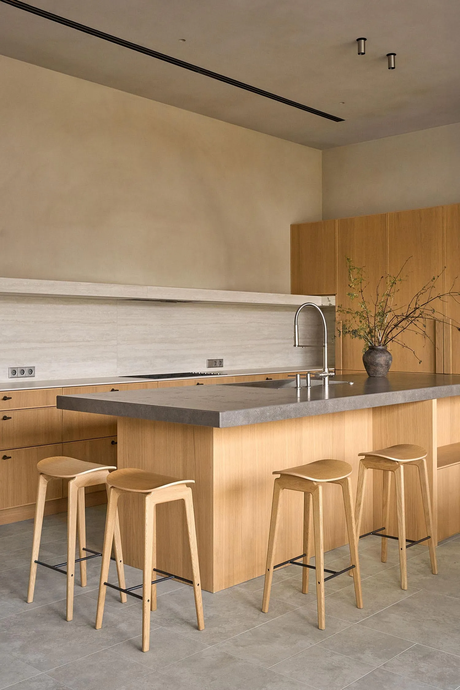 A modern kitchen with wooden cabinets, a marble countertop, and wooden stools, featuring a gray countertop and warm lighting