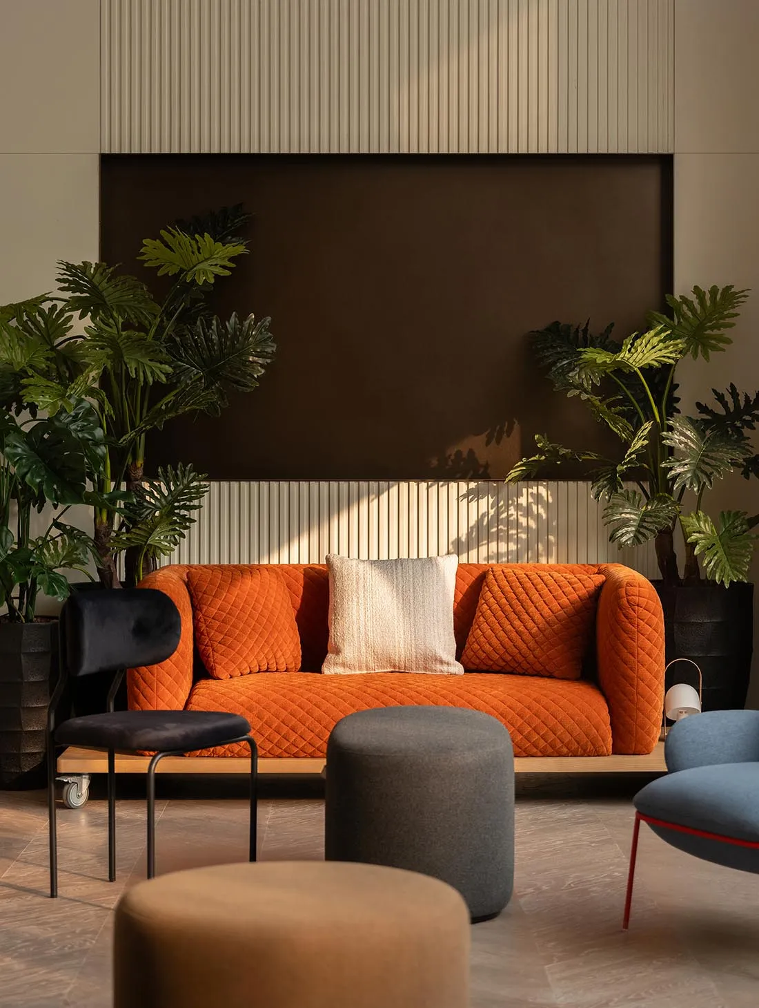 Cozy modern living space with an orange couch, a black chair, a potted plant, and a mounted TV in a well-lit room