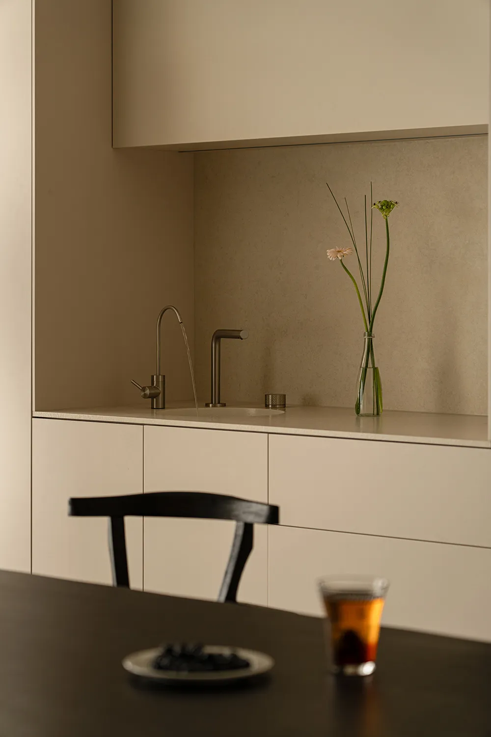 Modern kitchen with a marble counter, metal sink, and a vase with flowers, set against a natural light background