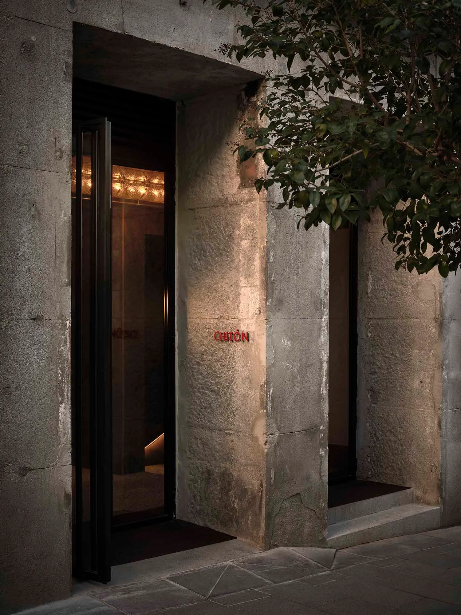 A modern building with a glass doorway and a window above, set against a concrete background with natural daylight