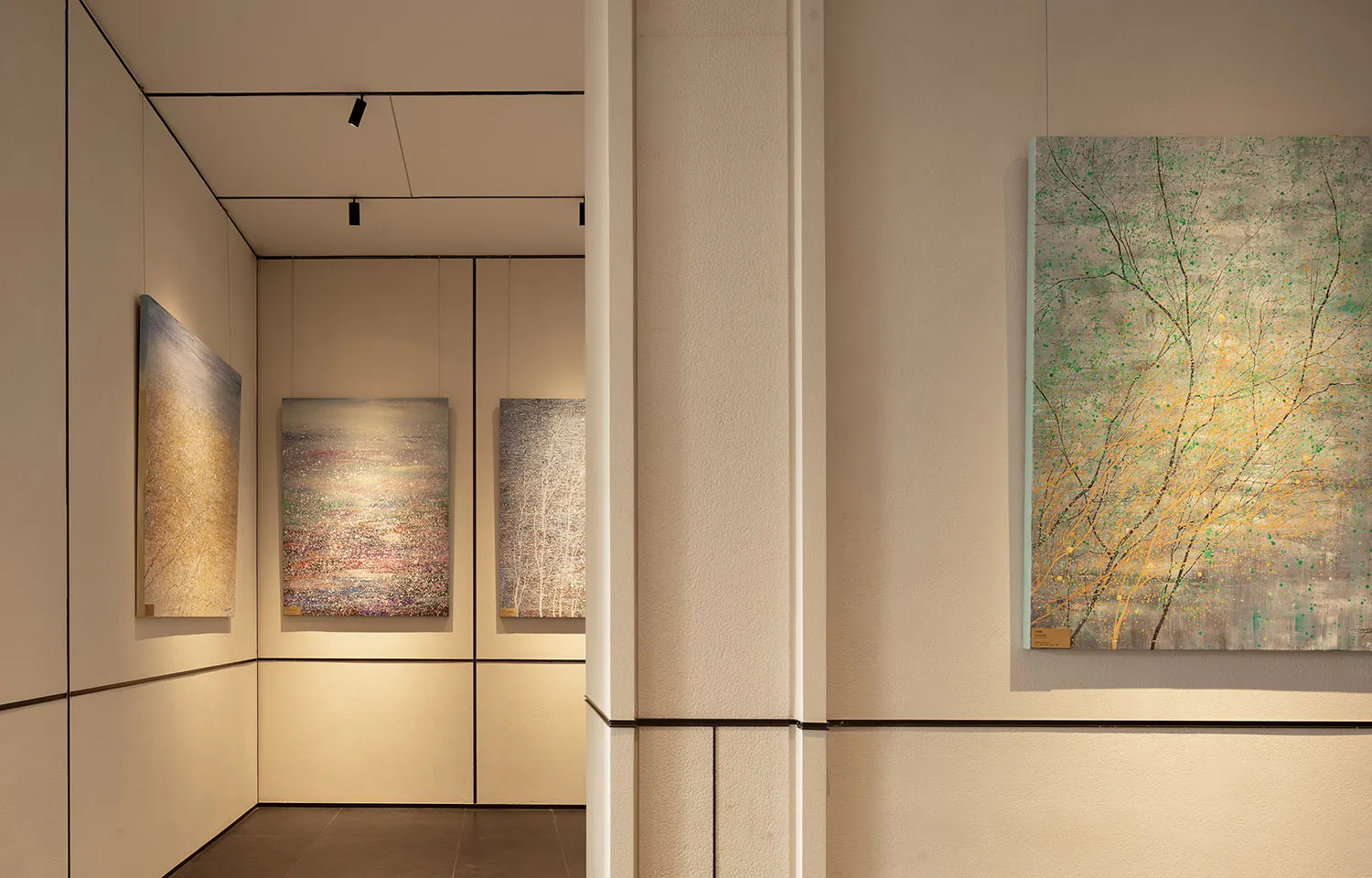 A room with white walls and a doorway, featuring three paintings on the wall and one on the door, in a clean and minimalistic space