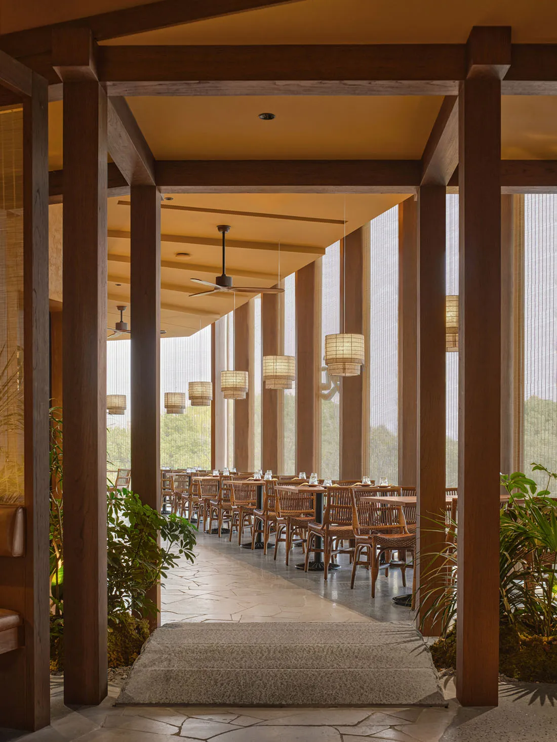 Warm and inviting restaurant interior with wooden furniture, multiple dining tables, and hanging lights