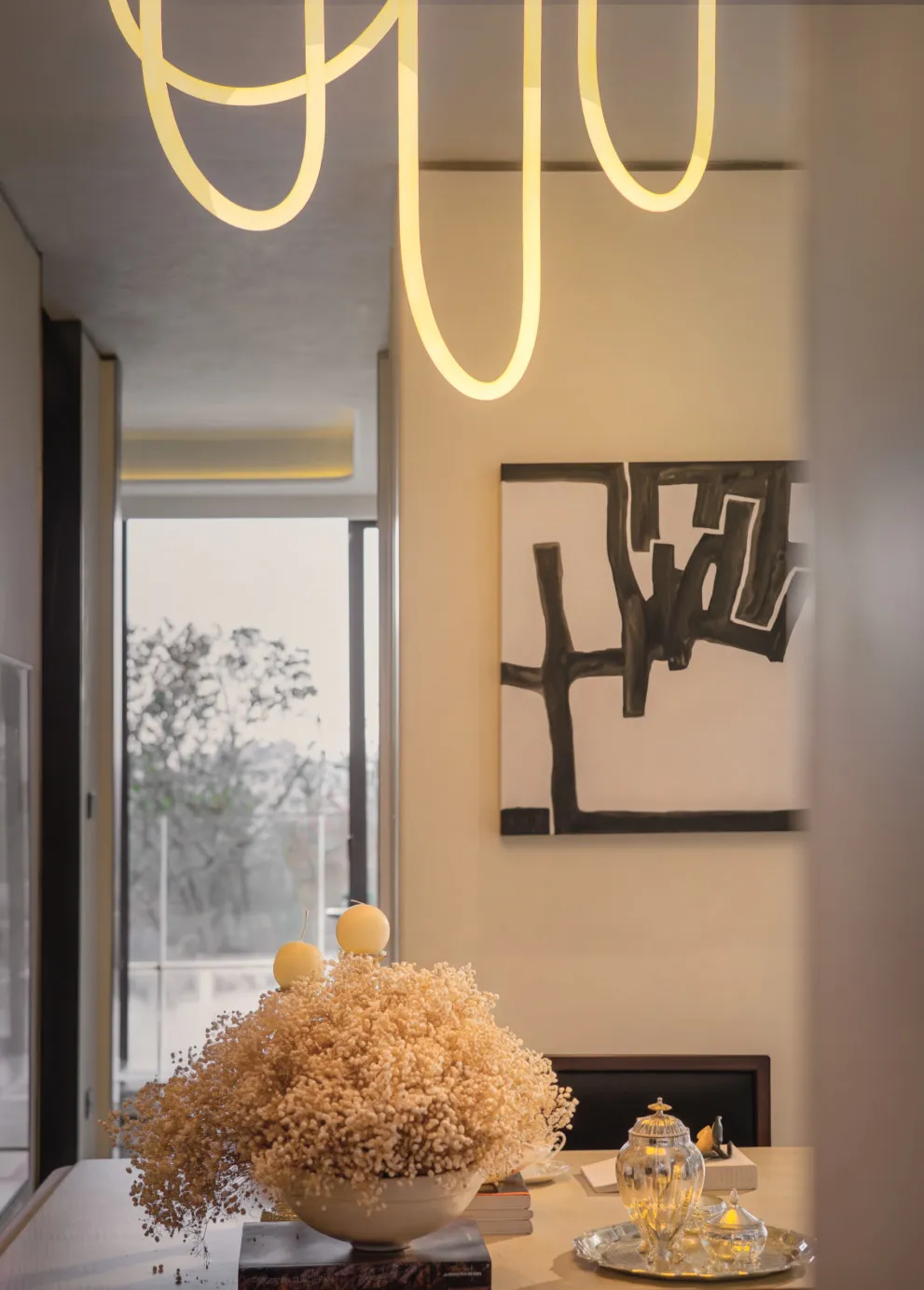 A dimly lit modern living space with a large pile of hay, chairs, and a dining table, filled with natural light