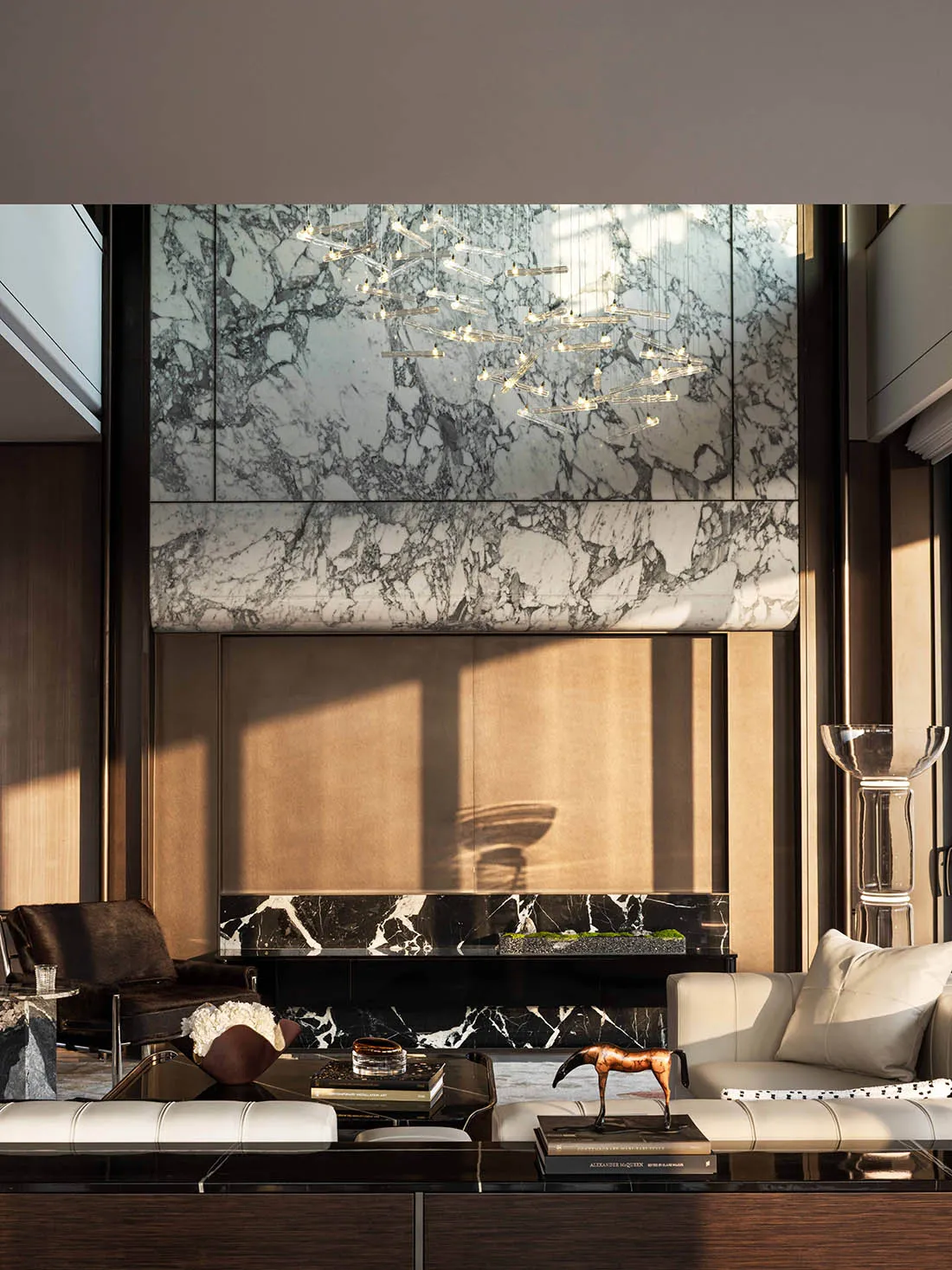 A modern living room with a marble fireplace, glass chandelier, and natural light from windows, featuring a couch, chair, and dining table