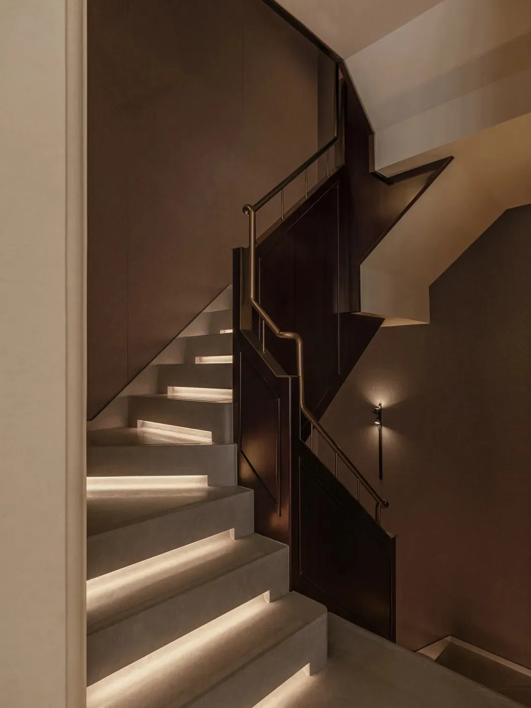 A wooden staircase with a metal railing in a well-lit hallway, captured from a perspective looking up the stairs