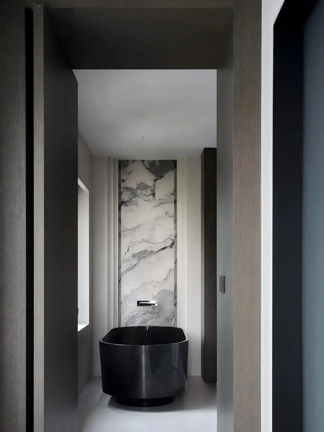 Black and white photograph of a modern bathroom with a black bathtub, toilet, and sink, set against a backdrop of marble walls in a dimly lit space