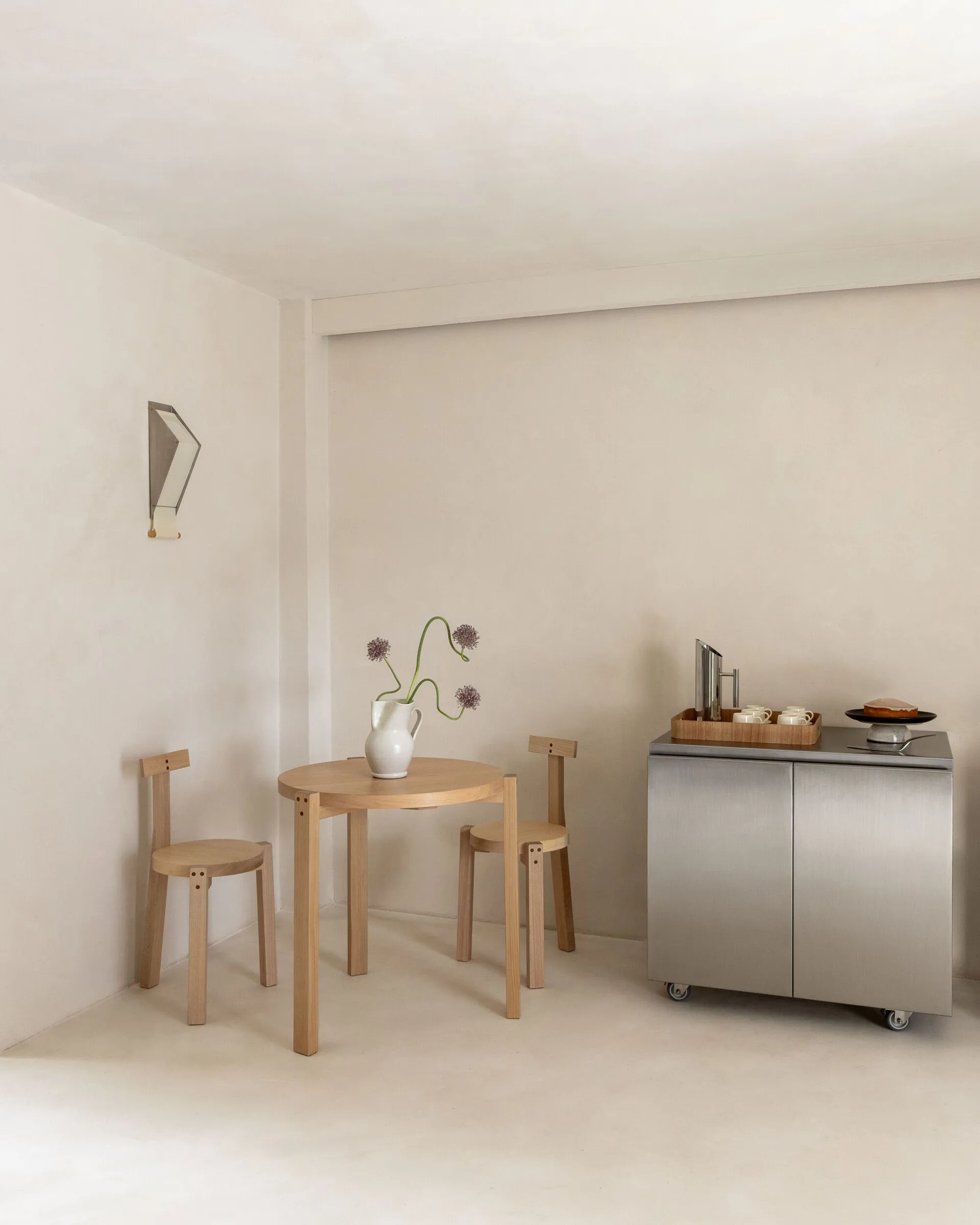 A modern kitchen with a dining table and chairs, surrounded by white cabinets, a sink, and a refrigerator, with natural light from the windows