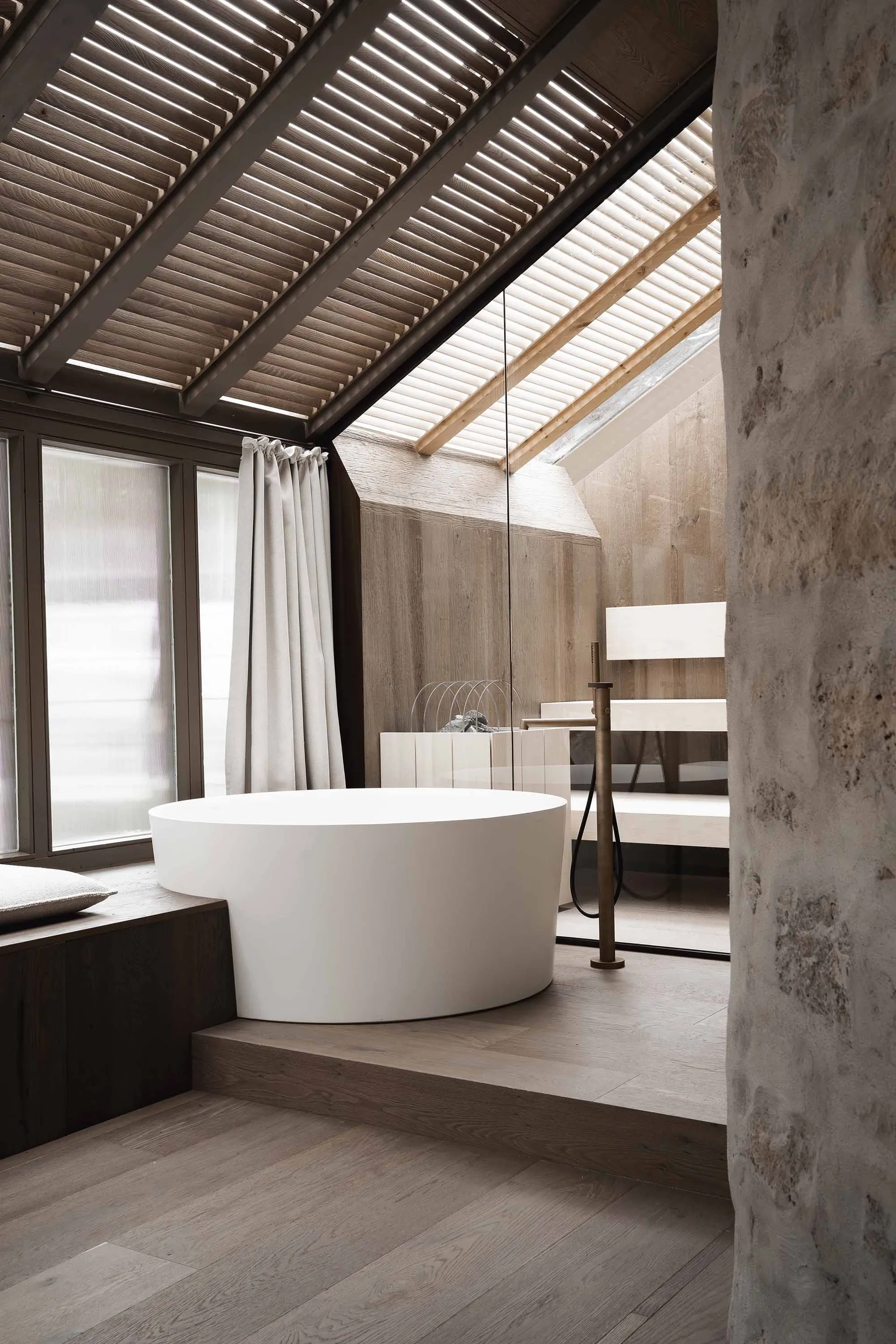 Bathroom with a white bathtub and shower, stone walls, and a wooden floor, in a dimly lit space creating a cozy atmosphere