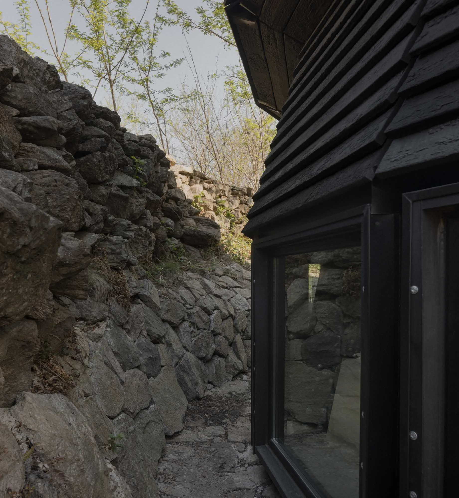 A traditional stone-built house with a black door and a window, set against a natural stone wall