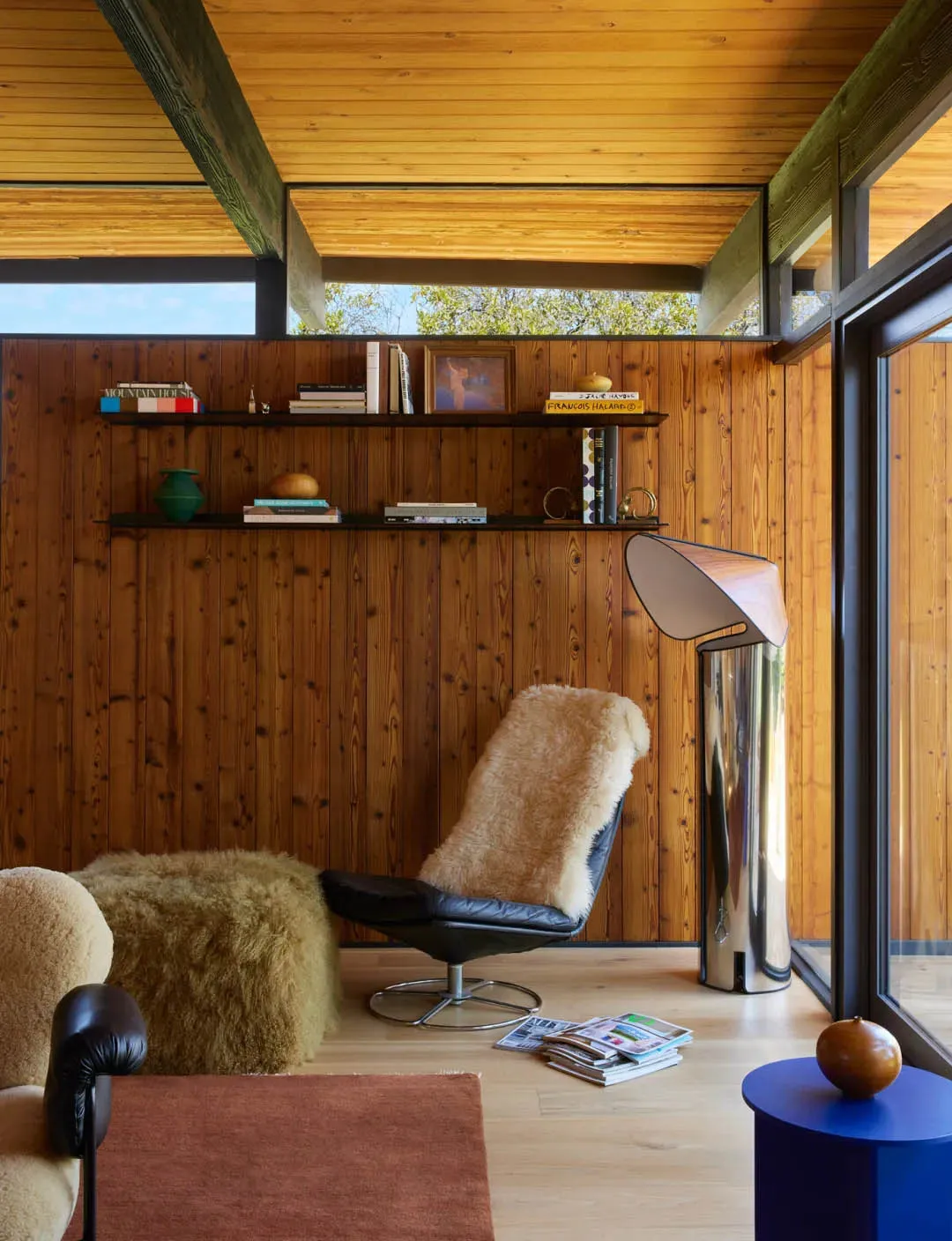 A cozy living room with wooden walls and floor, featuring a bookshelf, chair, and couch, with soft and diffused lighting