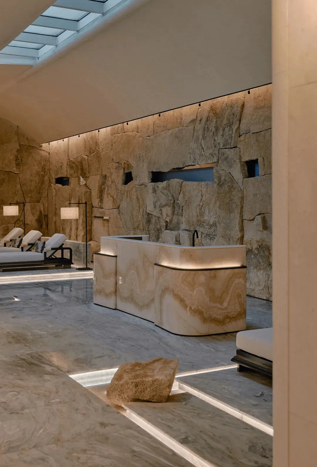 A well-lit room with a stone appearance, featuring a large stone wall, a stone bench, and a stone table, creating a warm and inviting atmosphere