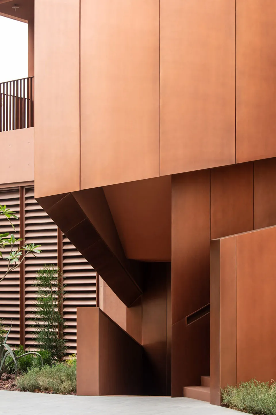 Photograph of a modern building with a brown metal facade, featuring a curved wall and a staircase leading up to the upper levels