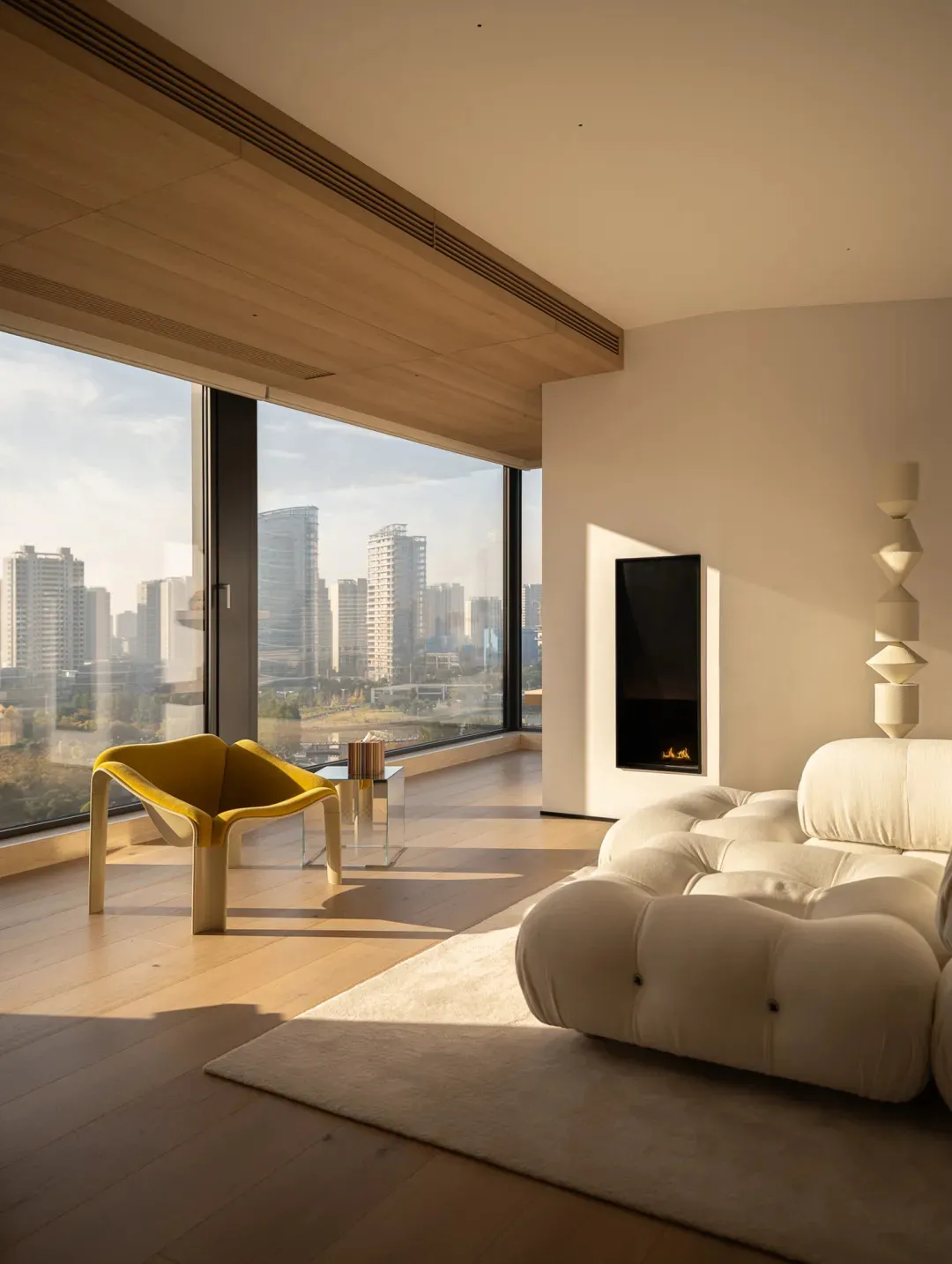 Cozy modern living room with a white couch, chair, and fireplace, lit by natural light from a large window with a city view